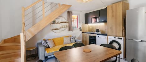 A modern kitchen with a wooden staircase, a dining area with a wooden table, and a sofa with cushions.