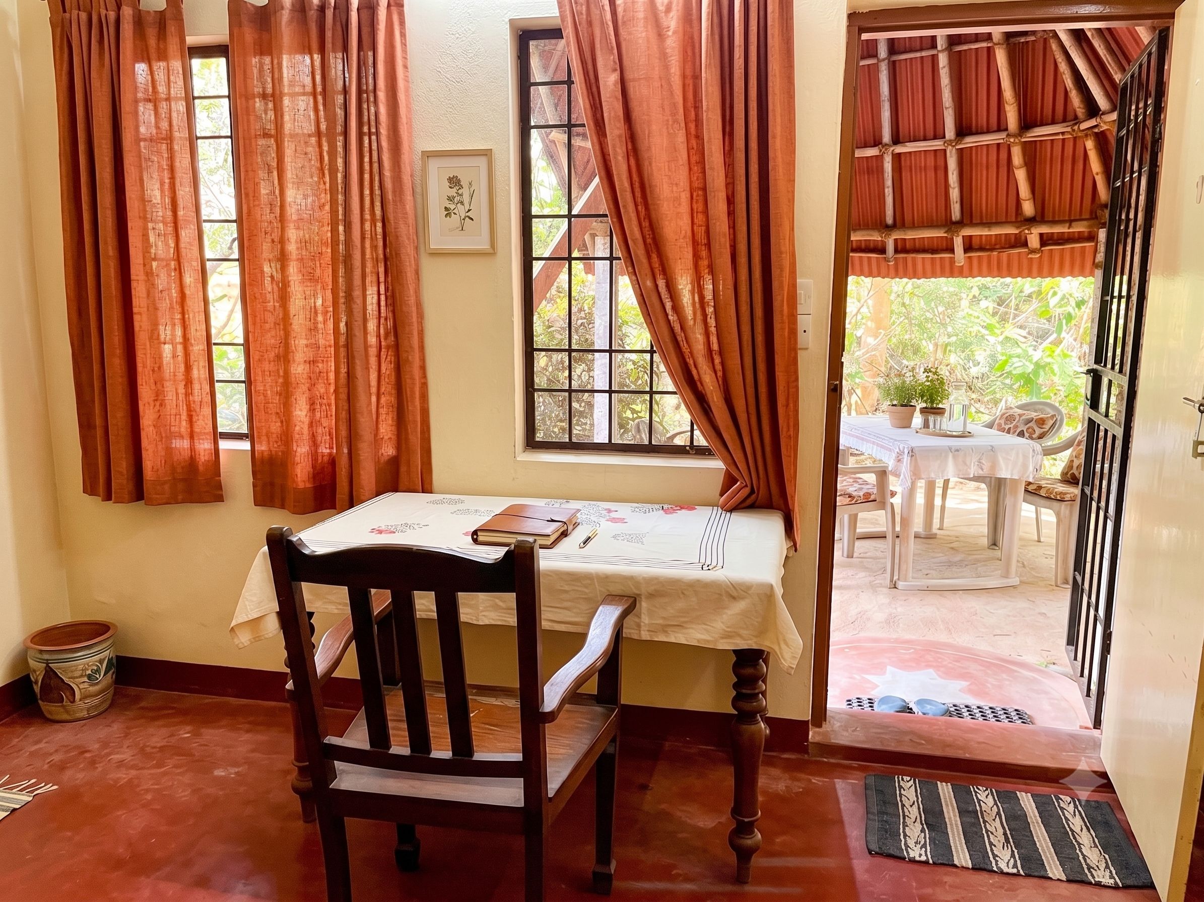 Una habitación con una silla de madera, una mesa con mantel blanco y una ventana con cortinas.