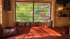 Habitació amb una finestra gran, una estanteria, un coixí i una prestatgeria penjada amb objectes decoratius.