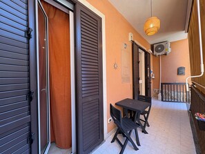 Ein Balkon mit Tisch und Stühlen, einer Hängelampe und einer Klimaanlage an der Wand.