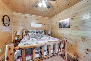 A wooden cabin bedroom with a bed, two bedside tables, a ceiling fan, and a framed sign on the wall. - Mammoth Cave Retreat w/ Hot Tub & Game Loft (Mammoth Cave)