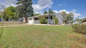 A single-story house with a porch, a fenced yard, and a large tree. - Walk to Prospect Lake! Quiet Home w/ Porch (Colorado Springs)