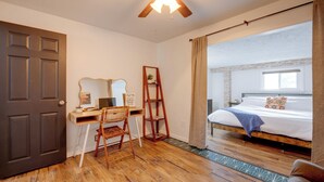A room with a wooden desk, a chair, a bed with a patterned bedspread, and a view of a brick wall through a window. - Walk to Prospect Lake! Quiet Home w/ Porch (Colorado Springs)