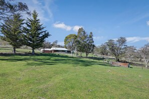 A rural property with a large open grassy area, a fenced paddock, and a building with a sloped roof.