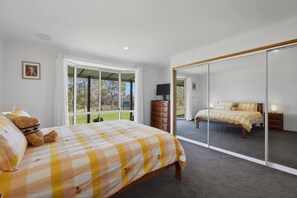 A bedroom with a bed, a teddy bear, a dresser, and a large mirror.