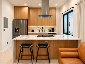 A modern kitchen with a marble countertop, stainless steel appliances, and wooden cabinetry. - Cozy Chic 2BR – New Kitchen, Complimentary Parking (Miami)