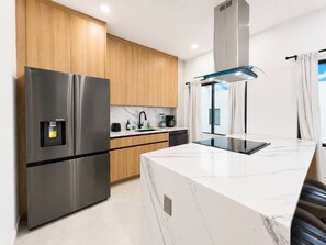 Eine moderne Küche mit Edelstahl-Kühlschrank, Holzschränken, einer Kücheninsel mit Marmorplatte und einem eingebauten Herd.