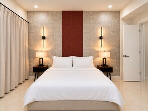 Ein Hotelzimmer mit einem großen Bett, zwei Nachttischen mit Lampen, einer Tür und einem Vorhang.