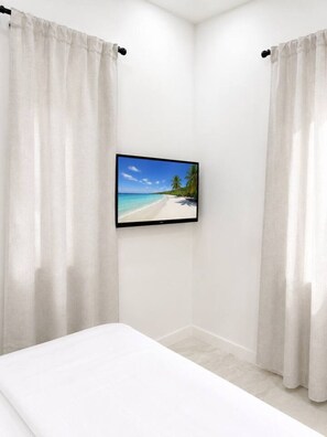 A bedroom with a bed, white curtains, and a framed picture of a beach scene on the wall. - Cozy Chic 2BR – New Kitchen, Complimentary Parking (Miami)