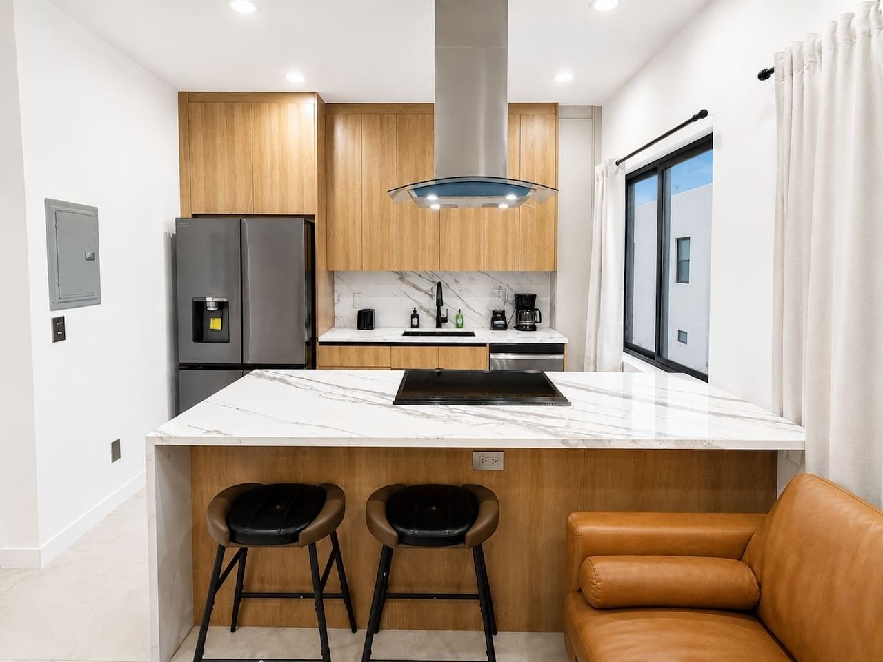 Cocina compacta con encimera de mármol, dos taburetes, una cafetera y vistas al exterior.