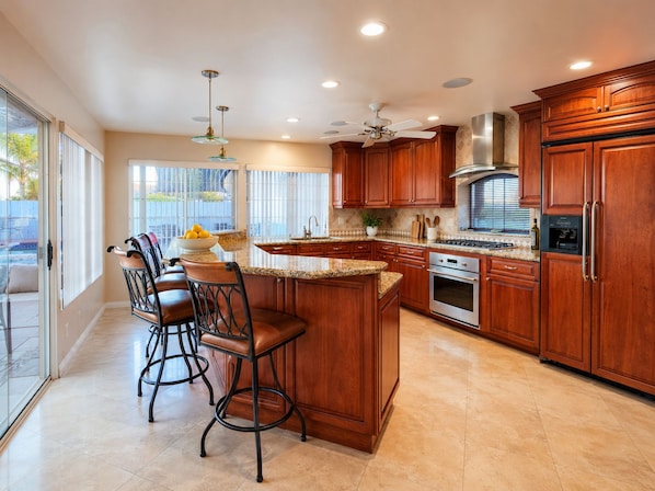 A kitchen with wooden cabinets, a central island with bar stools, a stainless steel range hood, and a built-in oven.