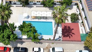 Vue aérienne d’un hôtel avec une piscine, des palmiers et un bâtiment au toit rouge.