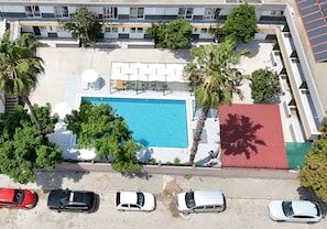 Vista aérea de um hotel com piscina, palmeiras e um edifício com telhado vermelho.