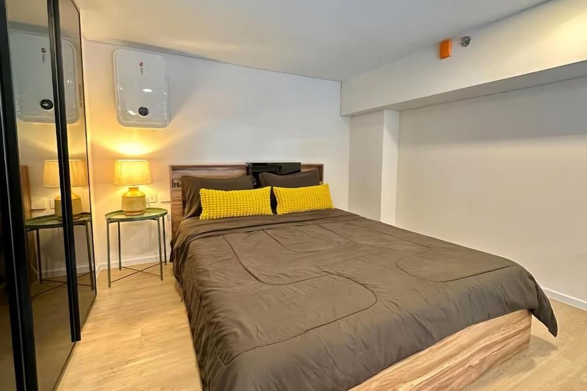 A bedroom with a bed, bedside tables, a mirror, and a wall-mounted light fixture.