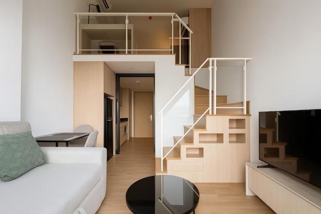A modern living room with a sofa, a coffee table, a TV, and a staircase.