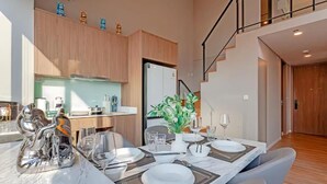 Een moderne eetruimte met een marmeren tafel gedekt voor vier personen, een keuken op de achtergrond en een trap die naar een hoger gelegen verdieping leidt.