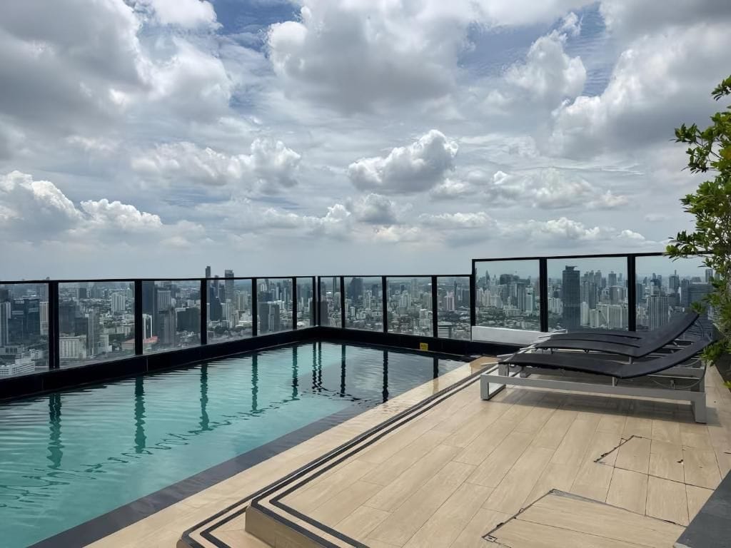 A rooftop infinity pool with a city skyline view, lounge chairs, and a clear sky.