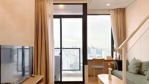Een moderne woonkamer met een flatscreen televisie, een bank, een eettafel en uitzicht op de stad door grote ramen.