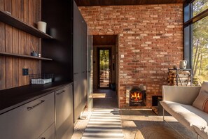 Une cuisine moderne avec une cheminée en briques, un canapé et une vue sur l’extérieur, visible à travers une porte vitrée.