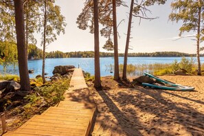 A wooden pathway leading to a sandy beach with a boat and trees. - Stay North - Vuohilahti (Valkeakoski)