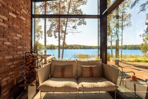Une pièce chaleureuse avec un mur en briques, un canapé confortable et une grande fenêtre donnant sur un lac et une forêt.