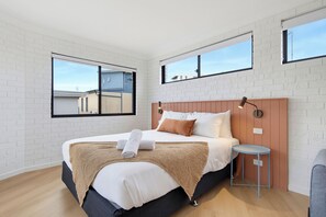 A modern bedroom with a large bed, a bedside table, and a window. - The Bay (Batemans Bay)