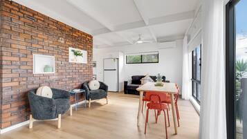 A modern interior with a brick wall, a dining area with red chairs, and a kitchen with white cabinets.