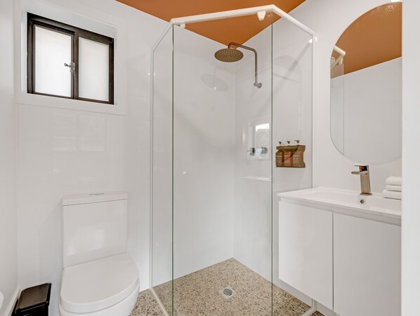 A modern bathroom with a glass-enclosed shower, a toilet, and a sink with a mirror. - The Bay (Batemans Bay)