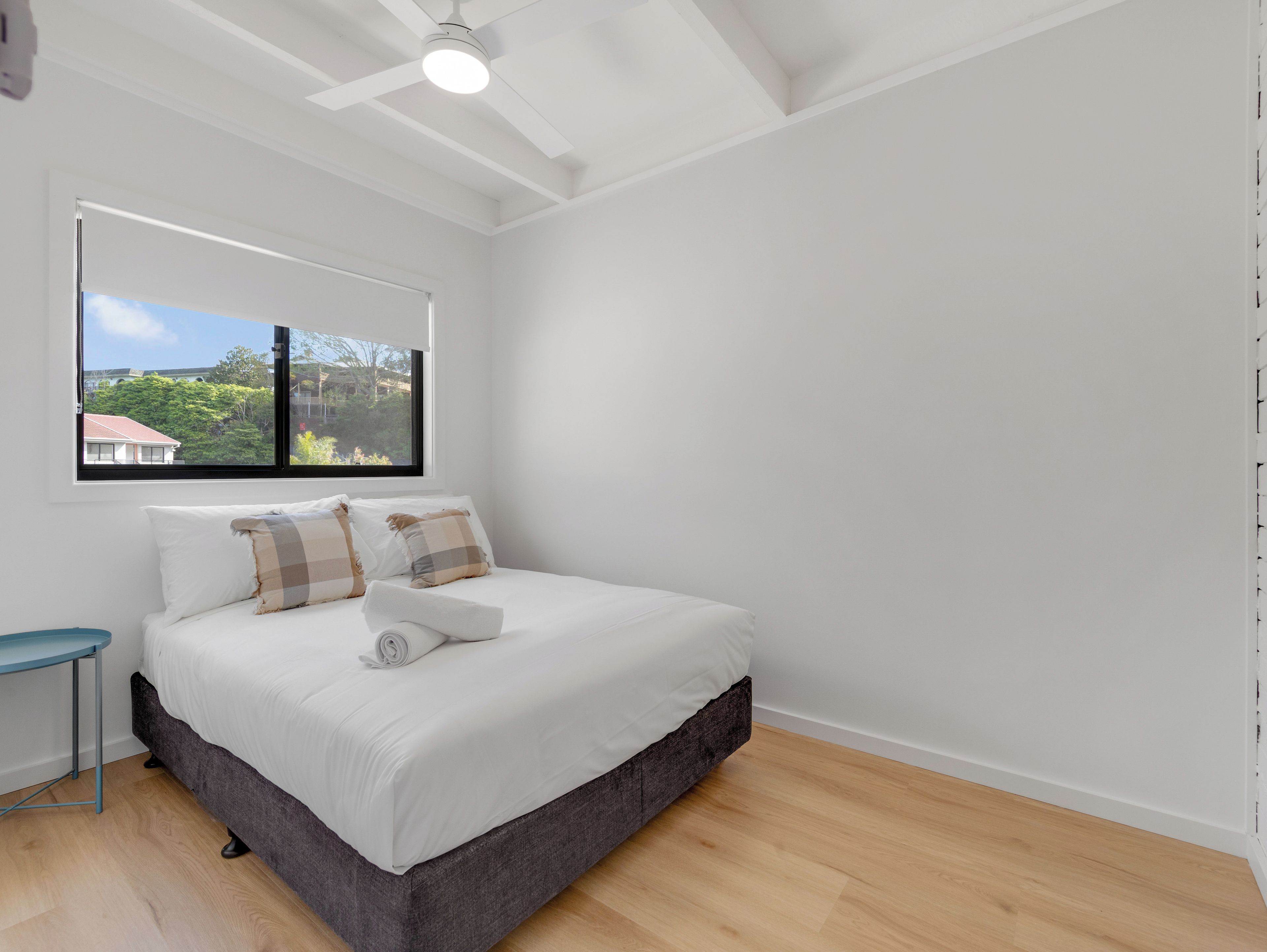 A bedroom with a bed, a window, and a view of a house and trees.