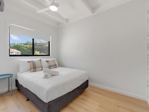Un dormitorio con cama, ventana y vista a una casa y árboles.