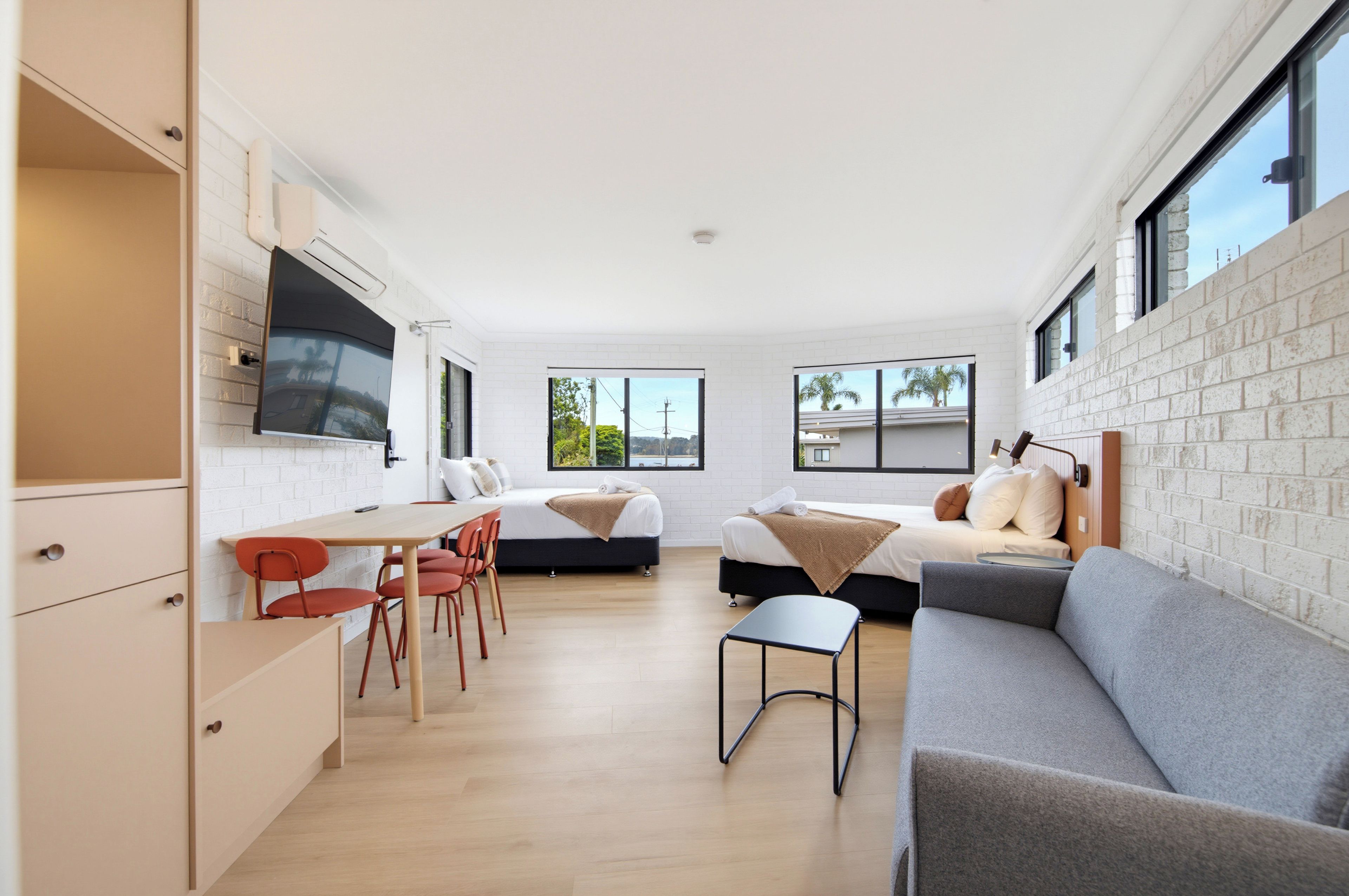 A modern, well-lit room with a dining area, two beds, and a sofa.