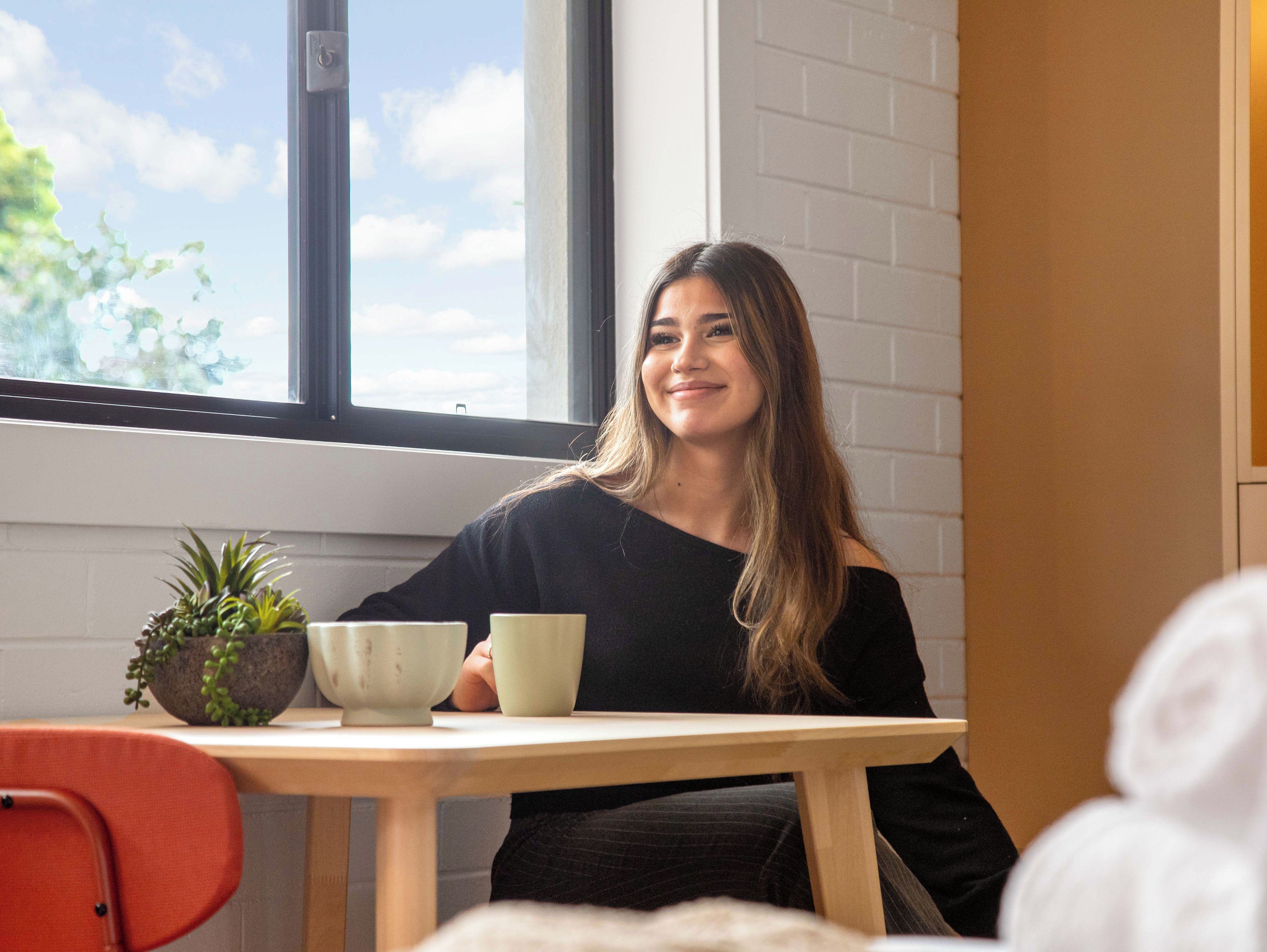 A person seated at a table with a window in the background.