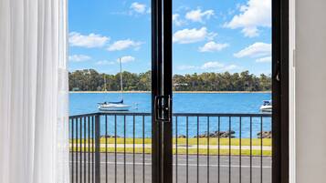 A view from a balcony with a railing, overlooking a body of water with boats, a beach, and a forested area.