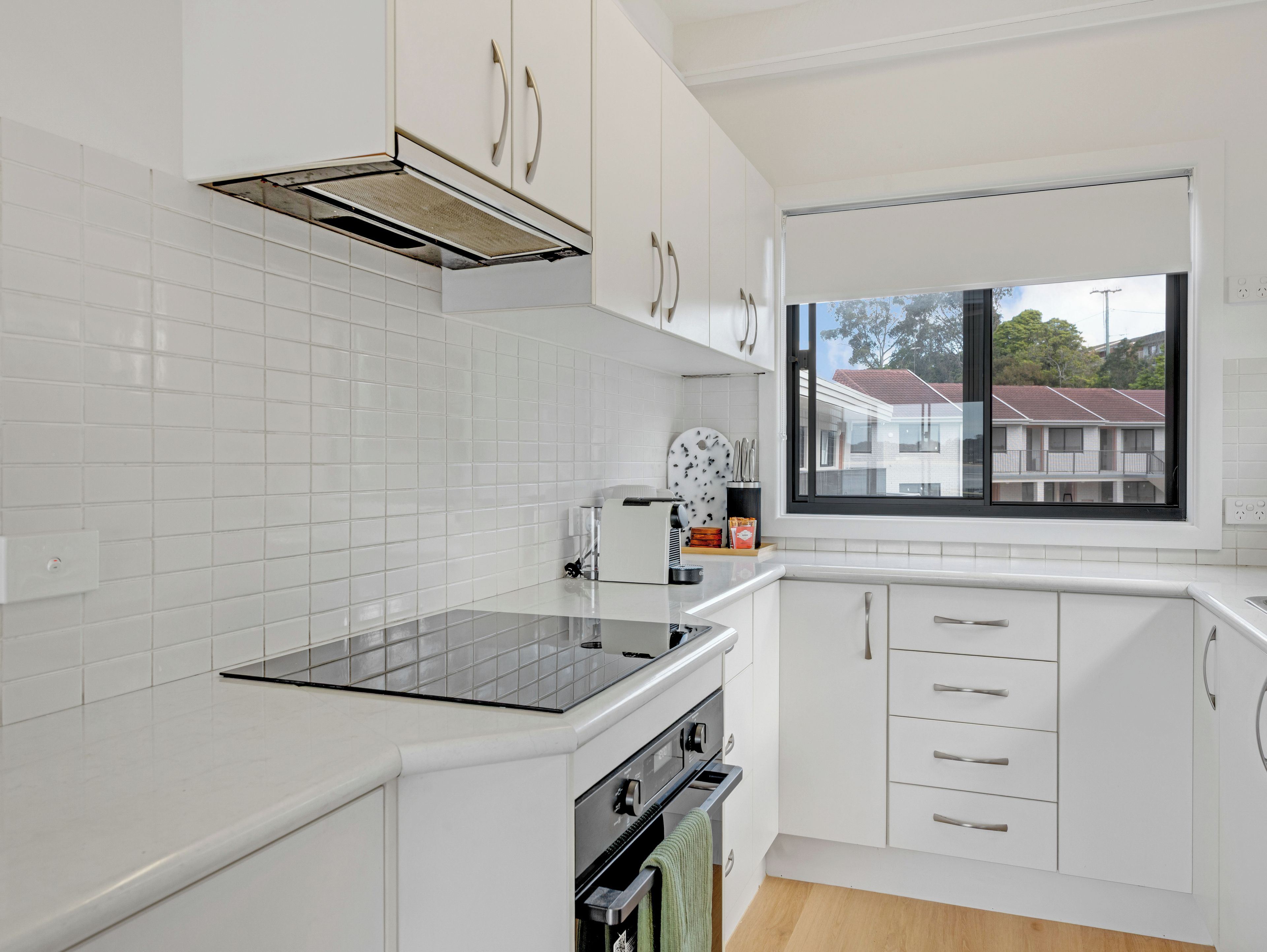 A modern kitchen with white cabinetry, a built-in oven, and a window with a view of residential buildings.
