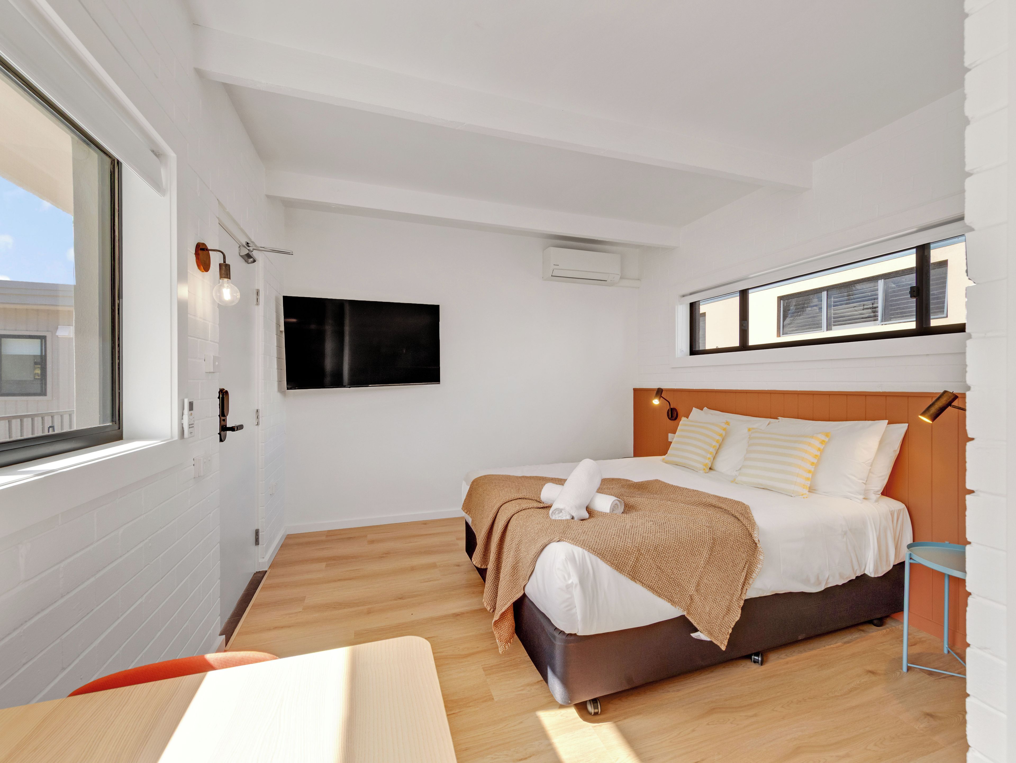 Ein modernes Schlafzimmer mit einem großen Bett, einem flachbildfernseher an der Wand und einem Fenster, das für natürliches Licht sorgt.