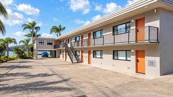 A multi-story motel with a parking area, a staircase, and a view of the ocean.