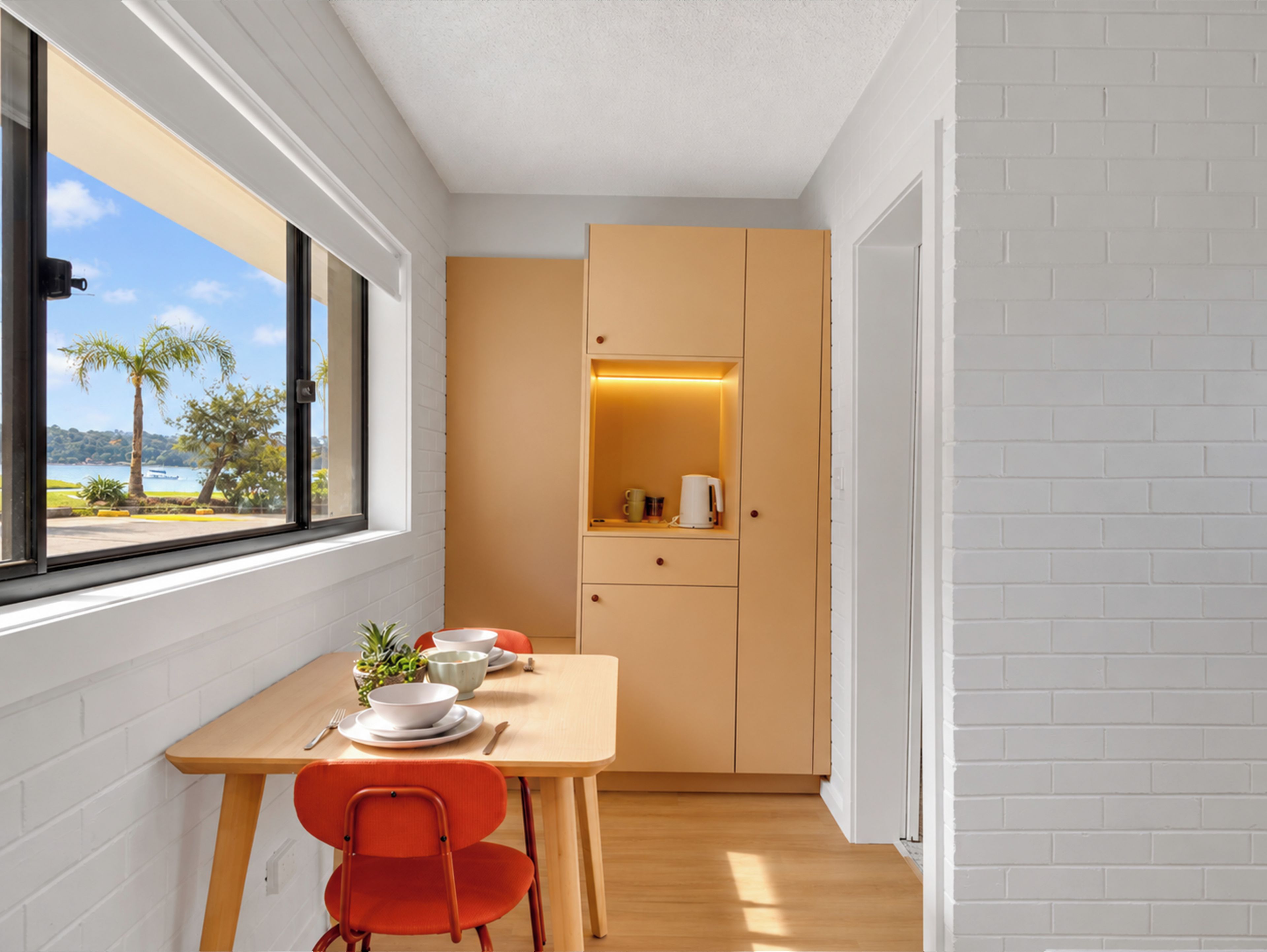 A compact kitchen with a dining area, a view of the outdoors, and a small cabinet with a light.