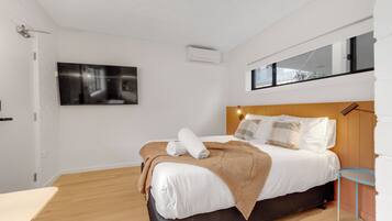 A modern bedroom with a bed, a flat-screen TV, and a window.
