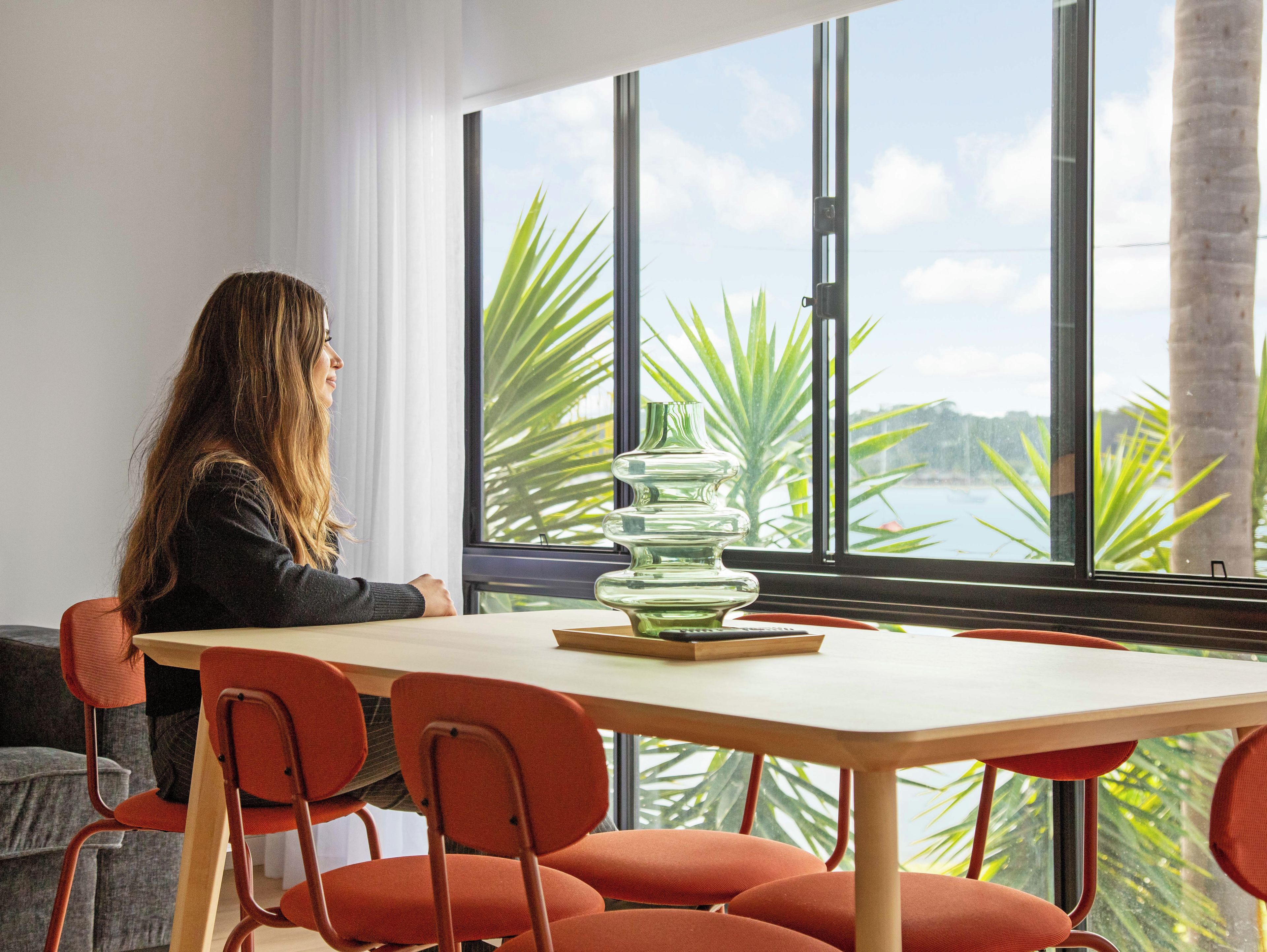A person seated at a table with a view of palm trees and a body of water through large windows.