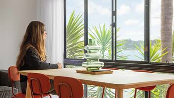 A person seated at a table with a view of palm trees and a body of water through large windows.