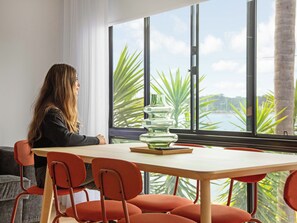 A person seated at a table with a view of palm trees and a body of water through large windows. - The Bay (Batemans Bay)
