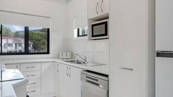 A modern kitchen with white cabinetry, a stainless steel dishwasher, and a window overlooking a residential area.