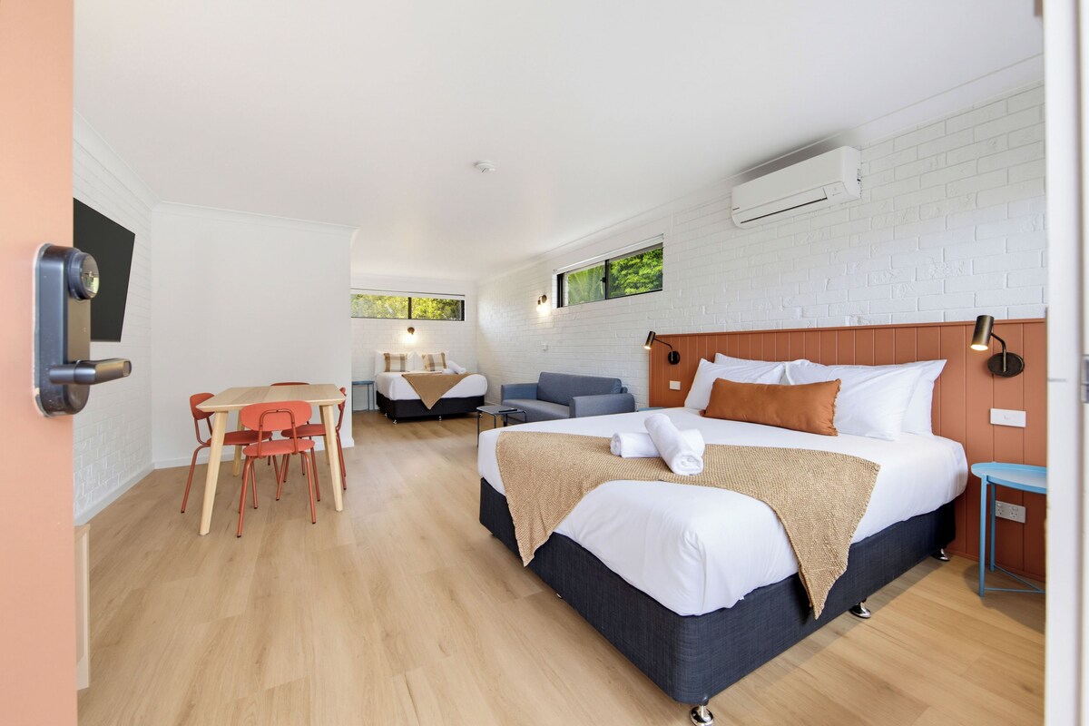 A modern hotel room with a bed, a desk, and a sofa.