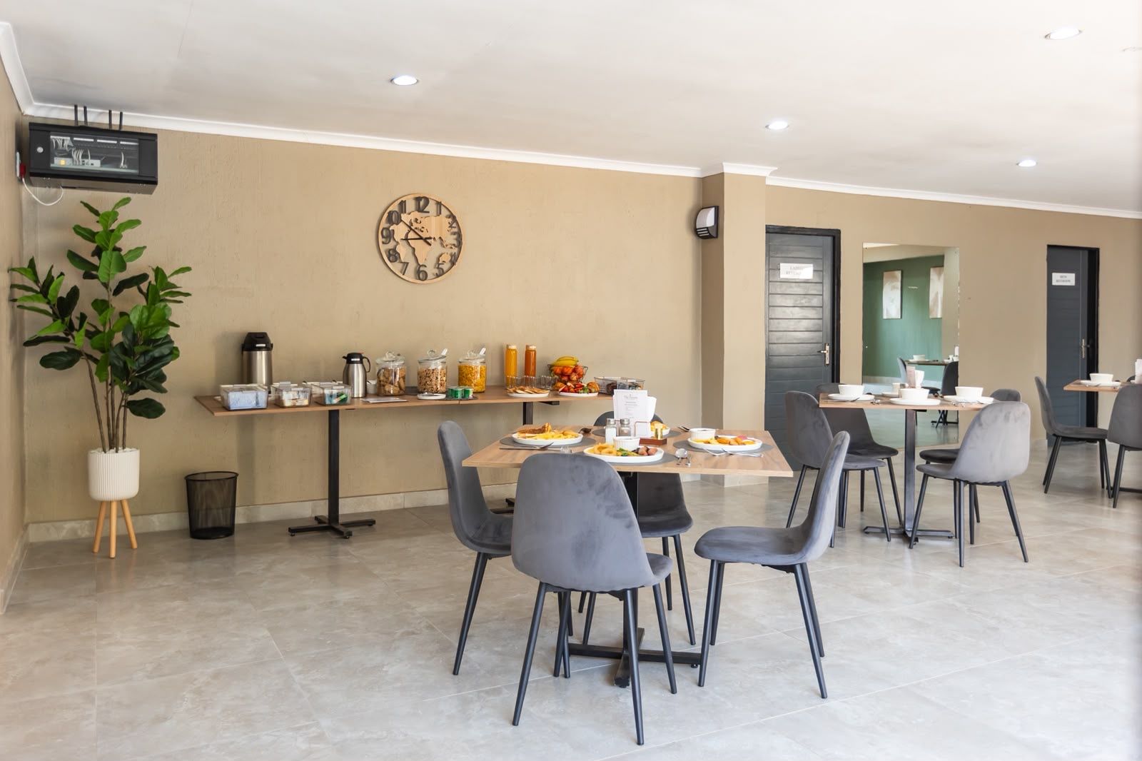 A modern dining area with a clock on the wall, a buffet setup, and a potted plant.