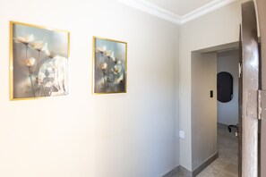 A hallway with two framed floral paintings on the wall, a door with a black circular object on the wall, and a tiled floor. - The Victoria Bed & Breakfast (Newcastle)