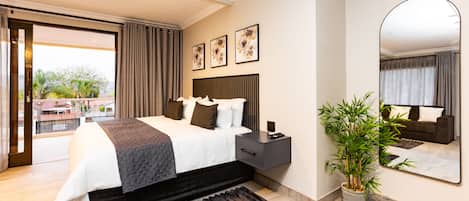 A modern hotel room with a large bed, a bedside table, a mirror, and a potted plant.