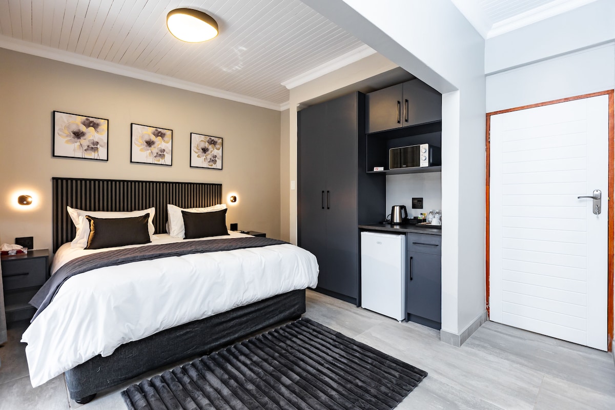 Un dormitorio moderno con cama, mesitas de noche, un escritorio, un armario y una kitchenette.