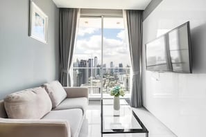 Ein modernes Wohnzimmer mit einer Couch, einem Couchtisch, einem Fernseher und einem großen Fenster mit Blick auf die Stadt.