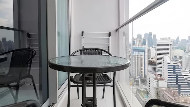 A balcony with a round table and chairs, a glass partition, and a city view. - Hyde 11 Sukhumvit Bangkok (Krung Thep Maha Nakhon)