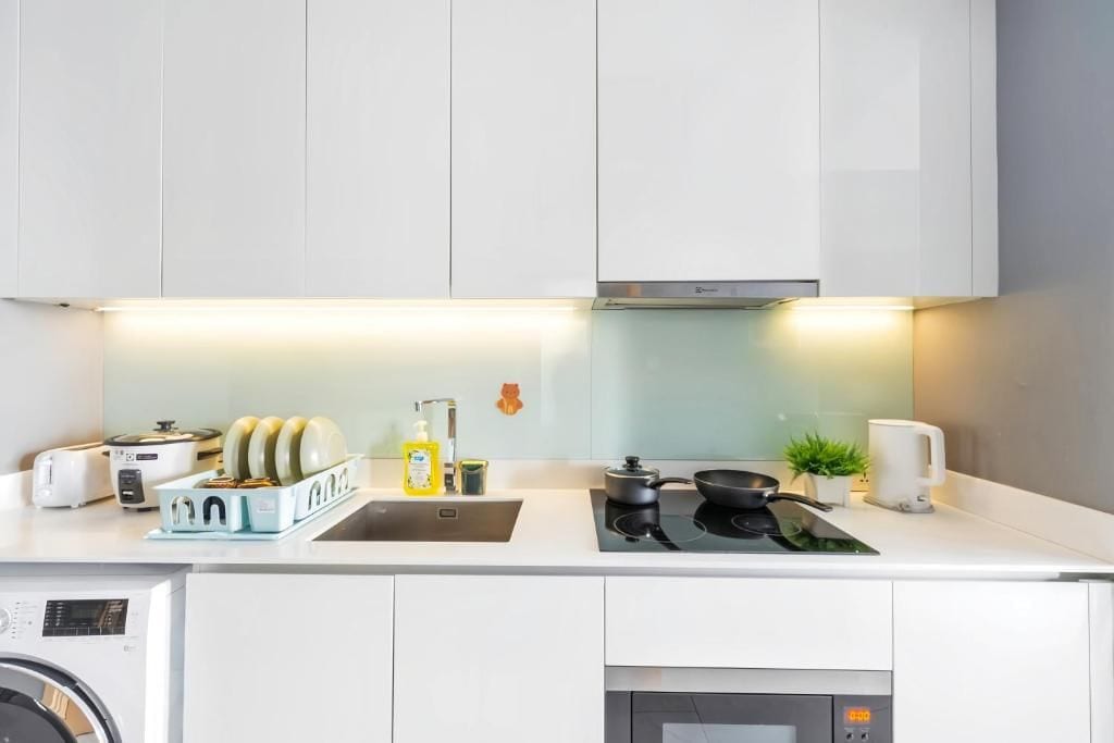 A modern kitchen with white cabinetry, a built-in washing machine, a stovetop, and a coffee maker.